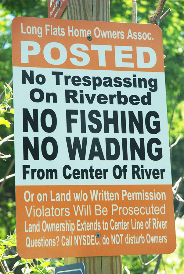 An orange and white sign says "Long Flats Home Owners Assoc. POSTED: No Trespassing on Riverbed. No Fishing No Wading From Center of River 